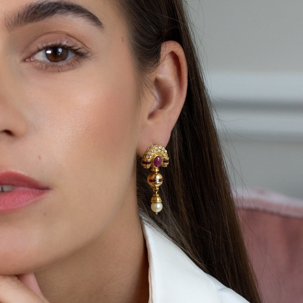 Woman wearing 1980s-1990s gold dangle earrings with pearl drops. 