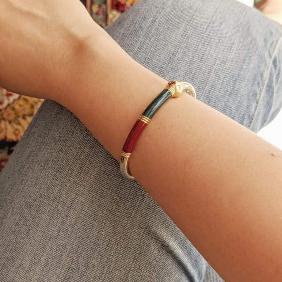 Plain gold bangle with red and green enamel worn on woman’s wrist.