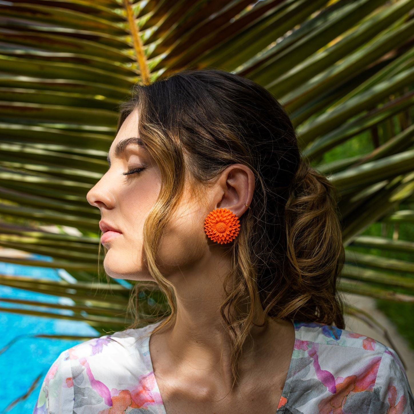 Woman in profile wearing orange flower clip-on earrings