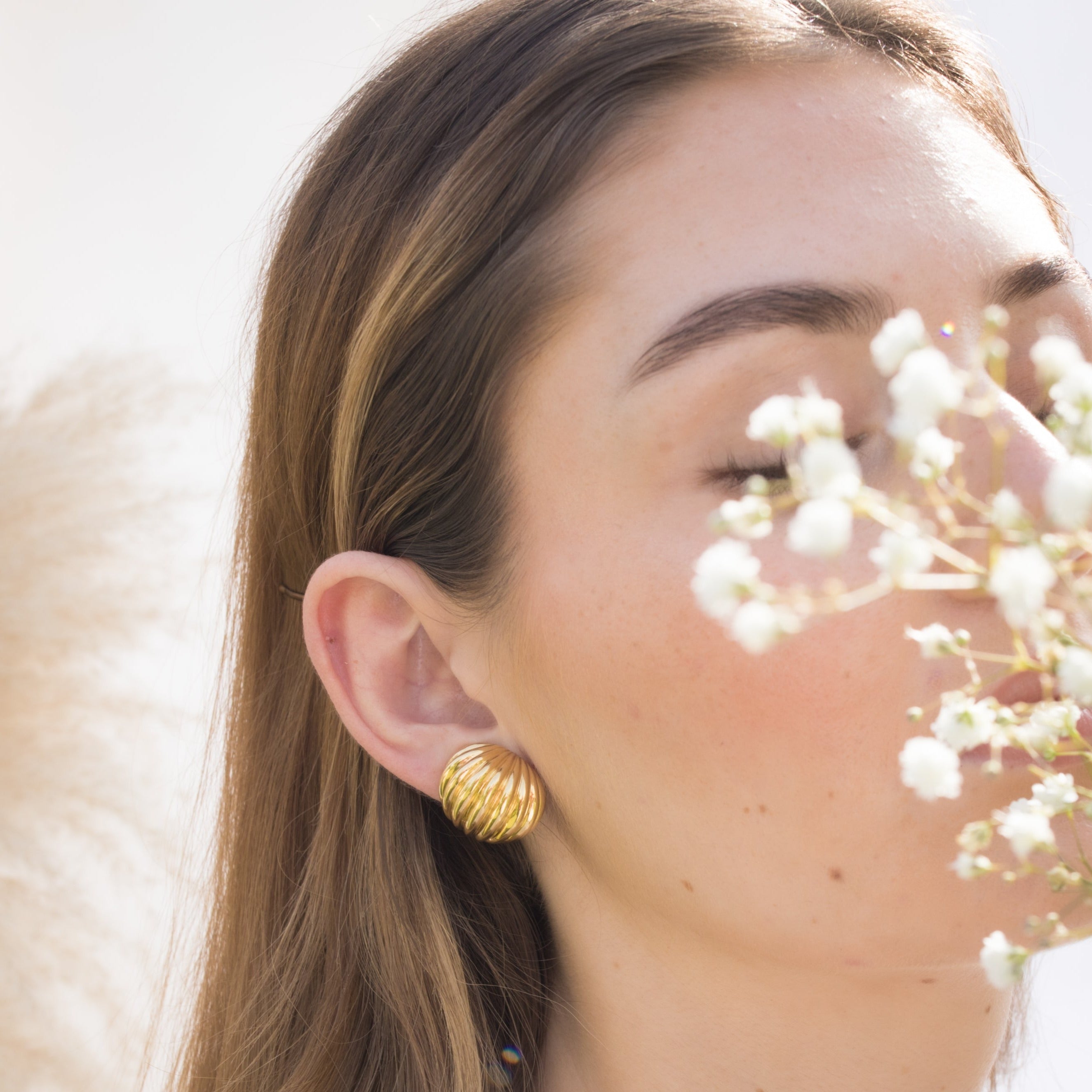 Vintage gold huggie earring worn on a woman’s ear.