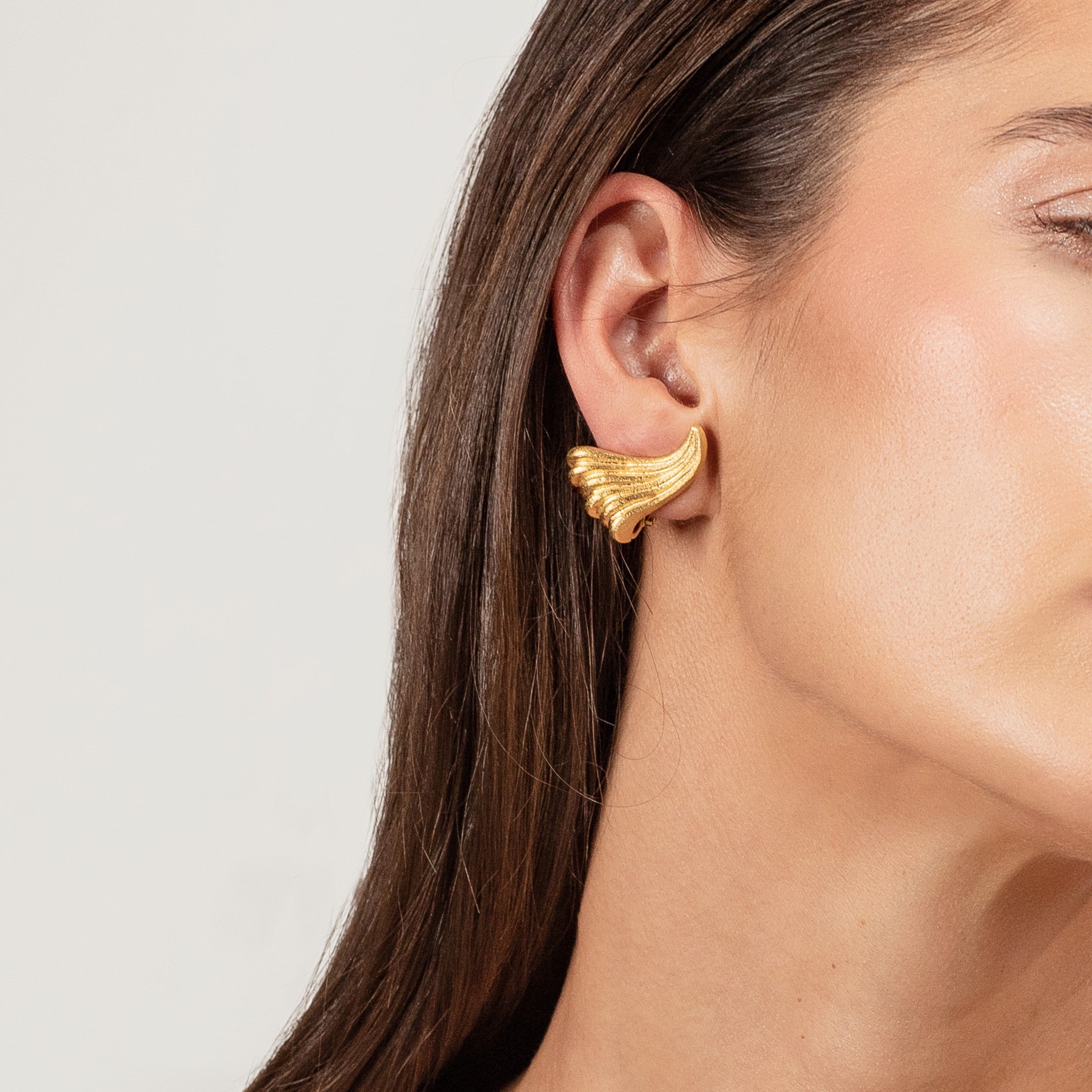  Vintage 18ct gold wave earrings worn on a woman’s ear.