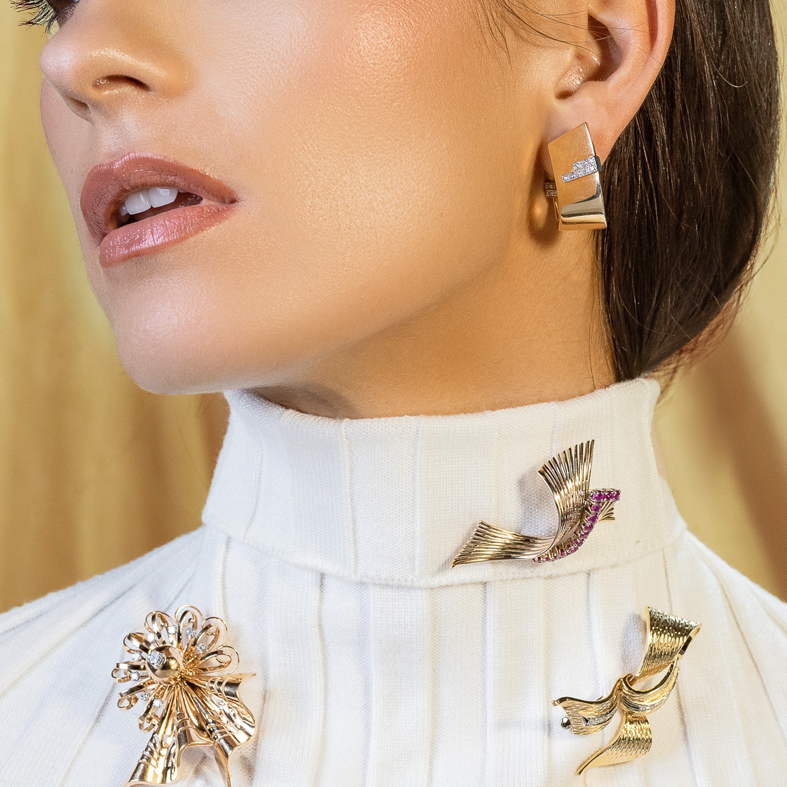 A collection of gold brooches worn on a woman’s white turtleneck sweater. 