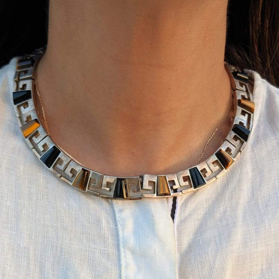 Collar-style onyx and tiger eye necklace worn on woman’s neck. 