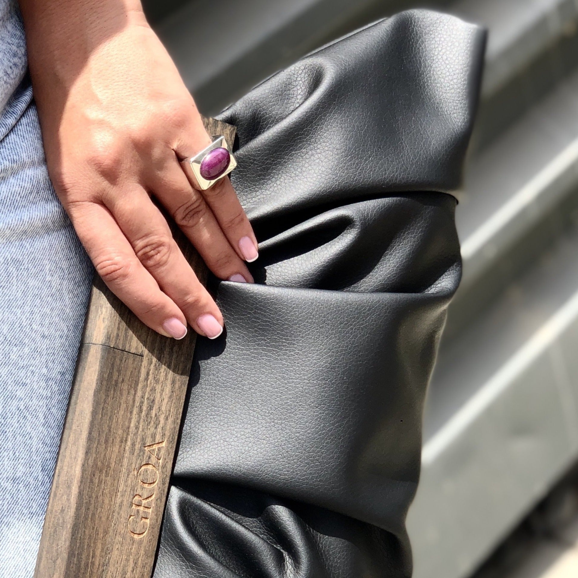 Woman’s hand holding a black bag and wearing a statement silver ring on the pinky finger. 
